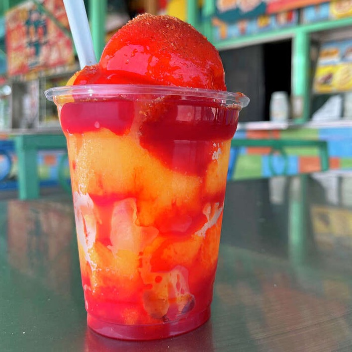 Mangonada cup layered with mango and red sauce, topped with a scoop and a straw